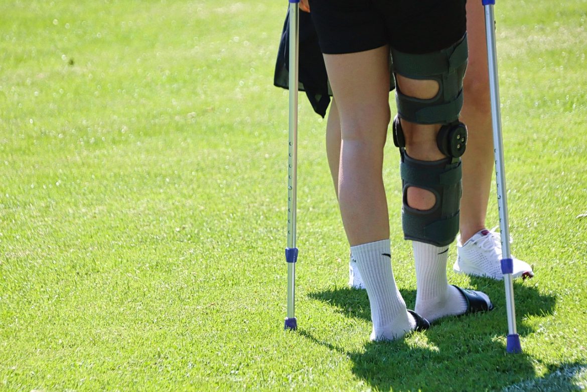 Osoba z opaską stabilizującą na kolanie poruszająca się o kulach po zabiegu ortopedycznym.